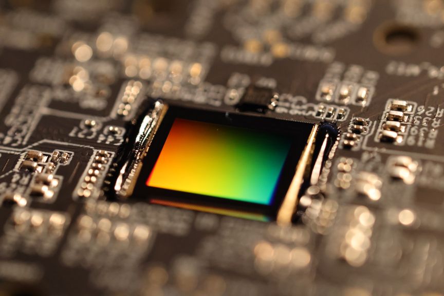 Nahaufnahme einer Leiterplatte mit einem quadratischen Bildsensor, der ein regenbogenfarbenes Schillern zeigt.